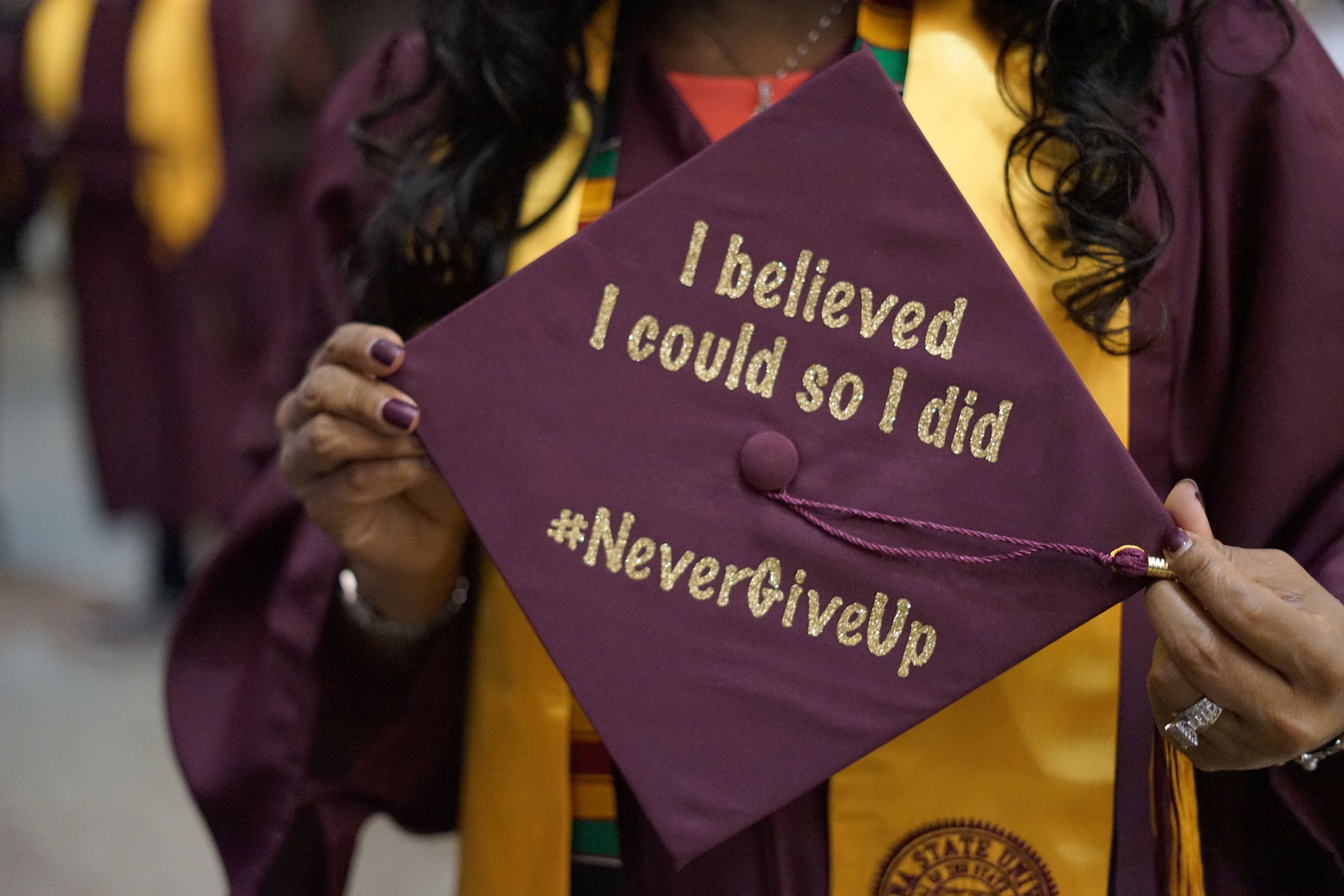 ASU student holds up custom graduation cap reading "I believed I could so I did #NeverGiveUp."