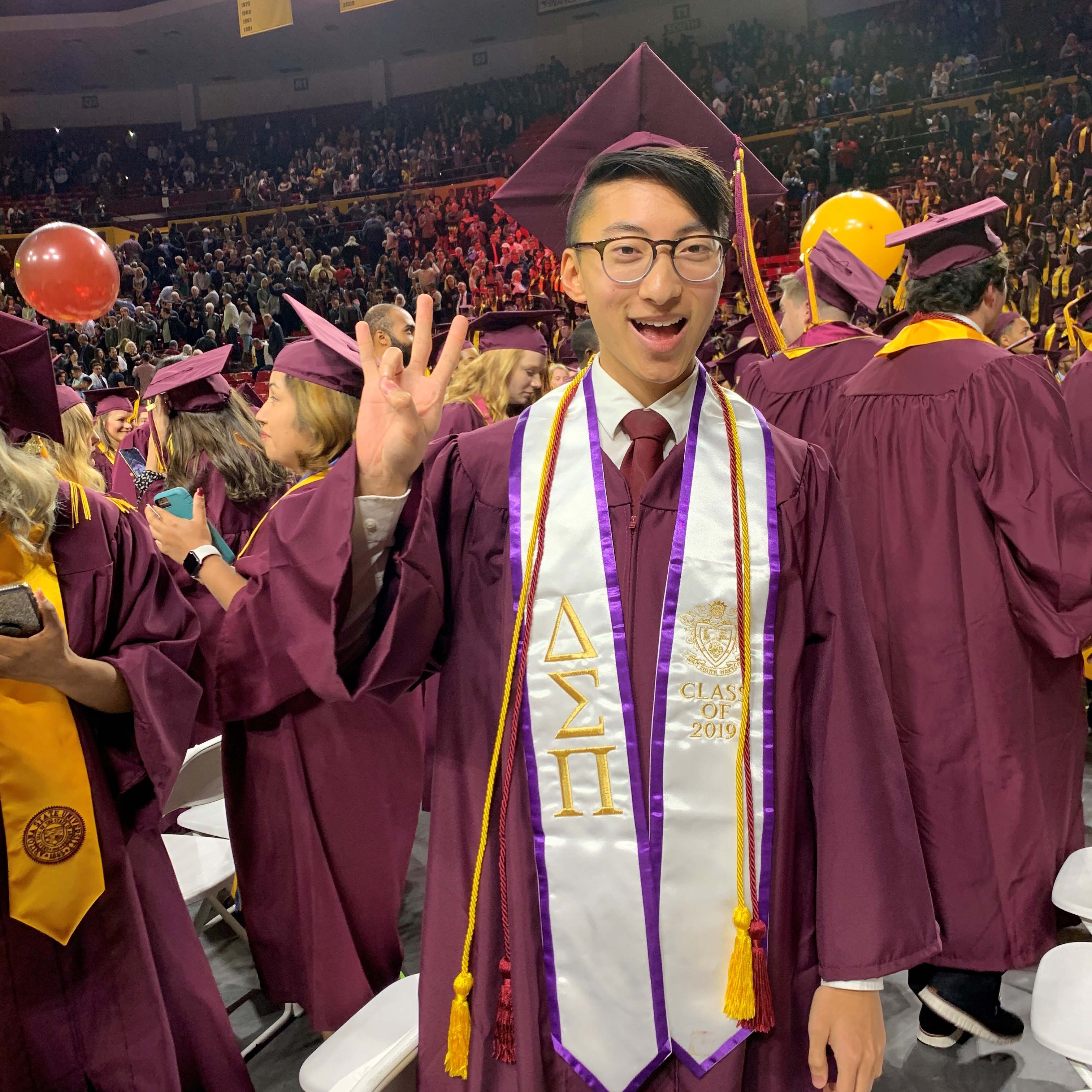 Bryan Pietsch doing a forks up symbol in his cap and gown at ASU graduation