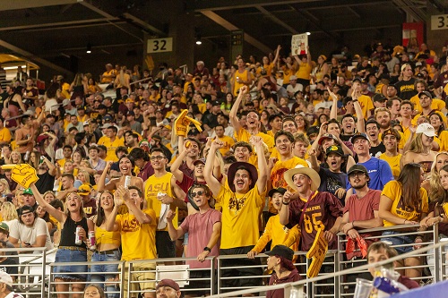 Hundreds of ASU students in gold cheer n the Inferno student section at Sun Devil Stadium