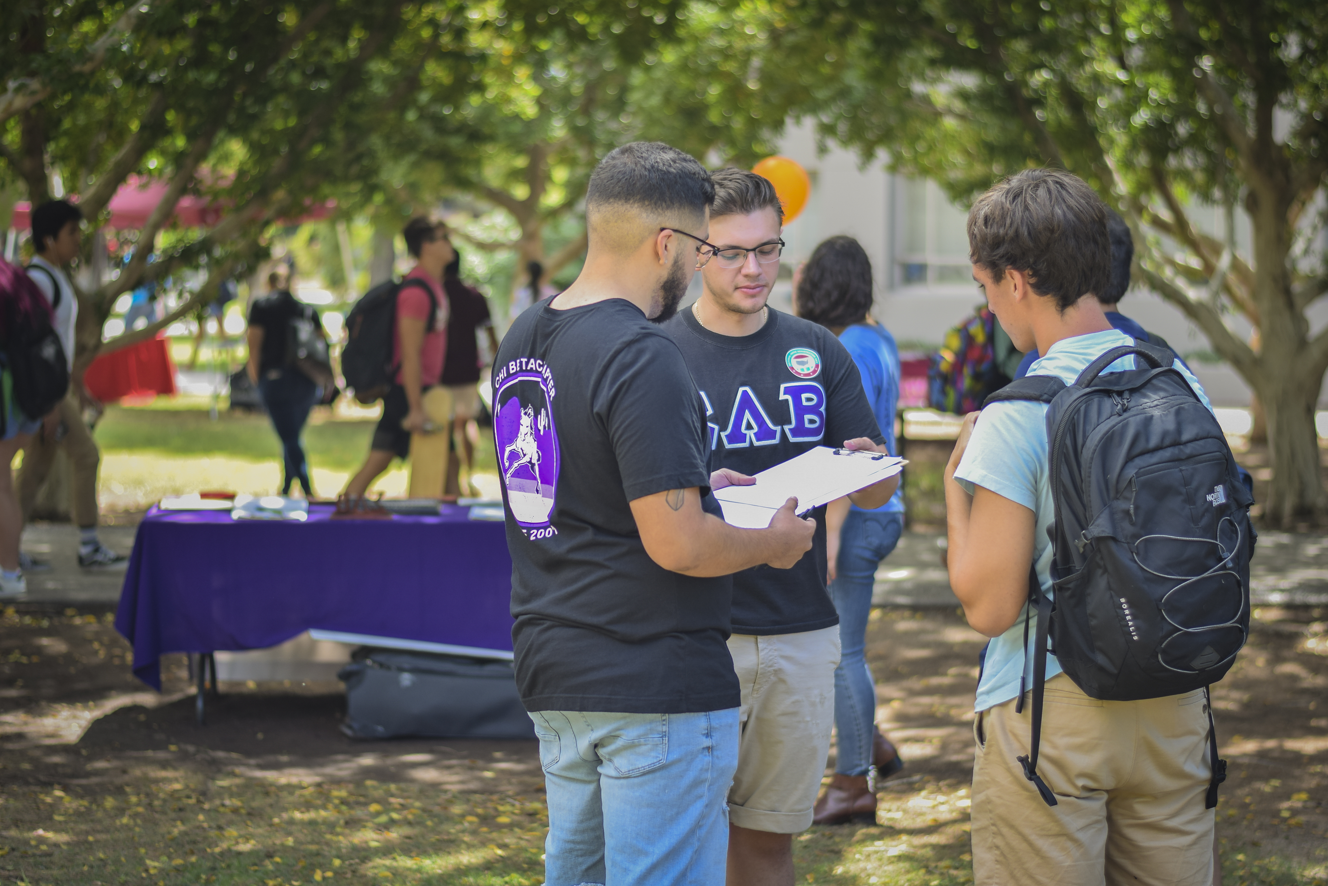 Three students, two with Greek-lettered shirts, talk with clipboards at National Voter Registration Day at ASU Tempe