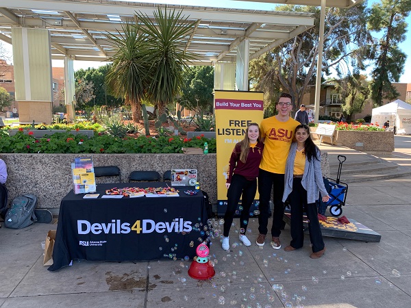 Three ASU students in front of a Devils 4 Devils table with a bubble machine