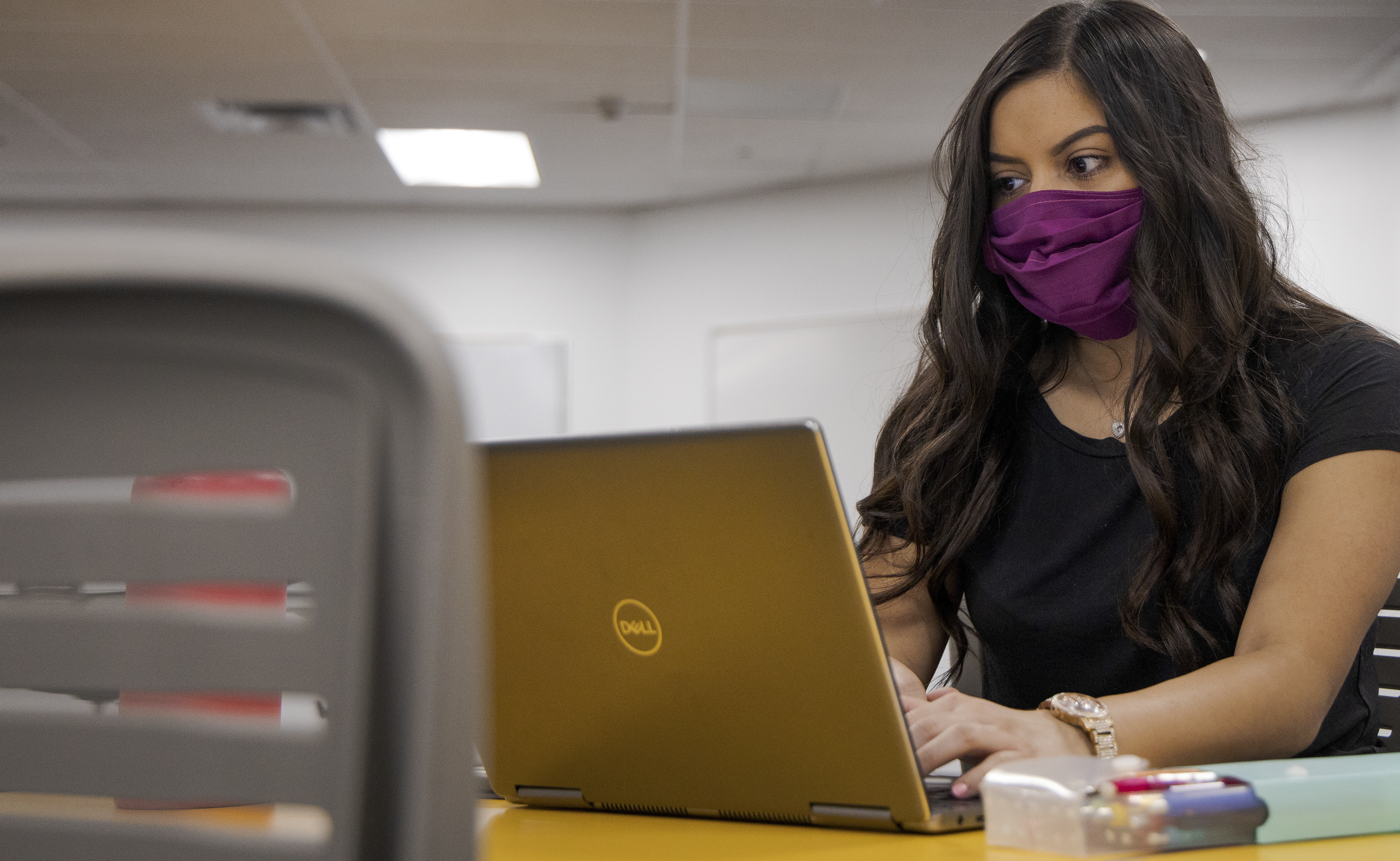 Female ASU student uses her computer while wearing a mask. 