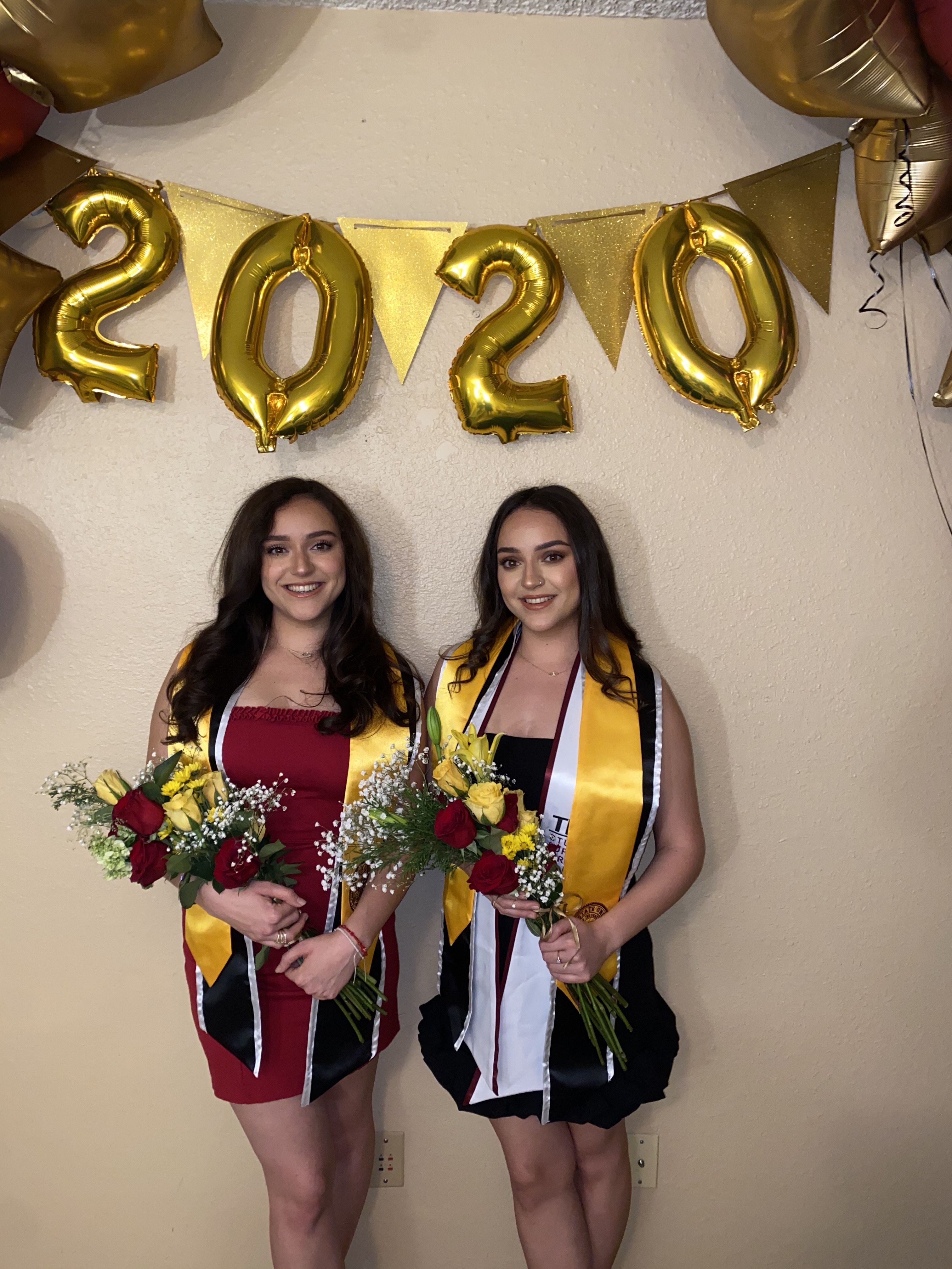 ASU twins Anahi and Sarahi Montano pose in front of graduation set up with balloons and flowers. 