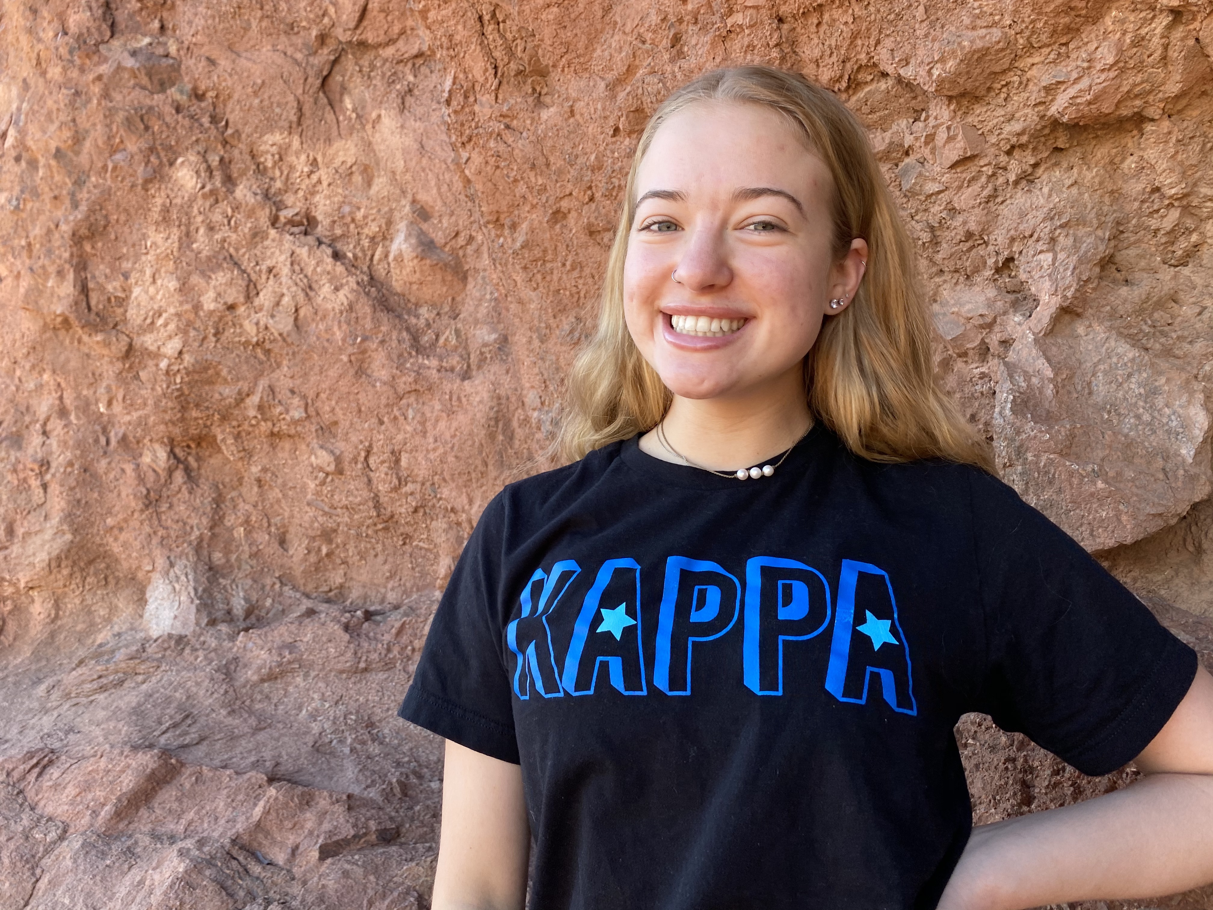Camrynne Karr, a student at ASU, smiles and poses behind a mountain.  