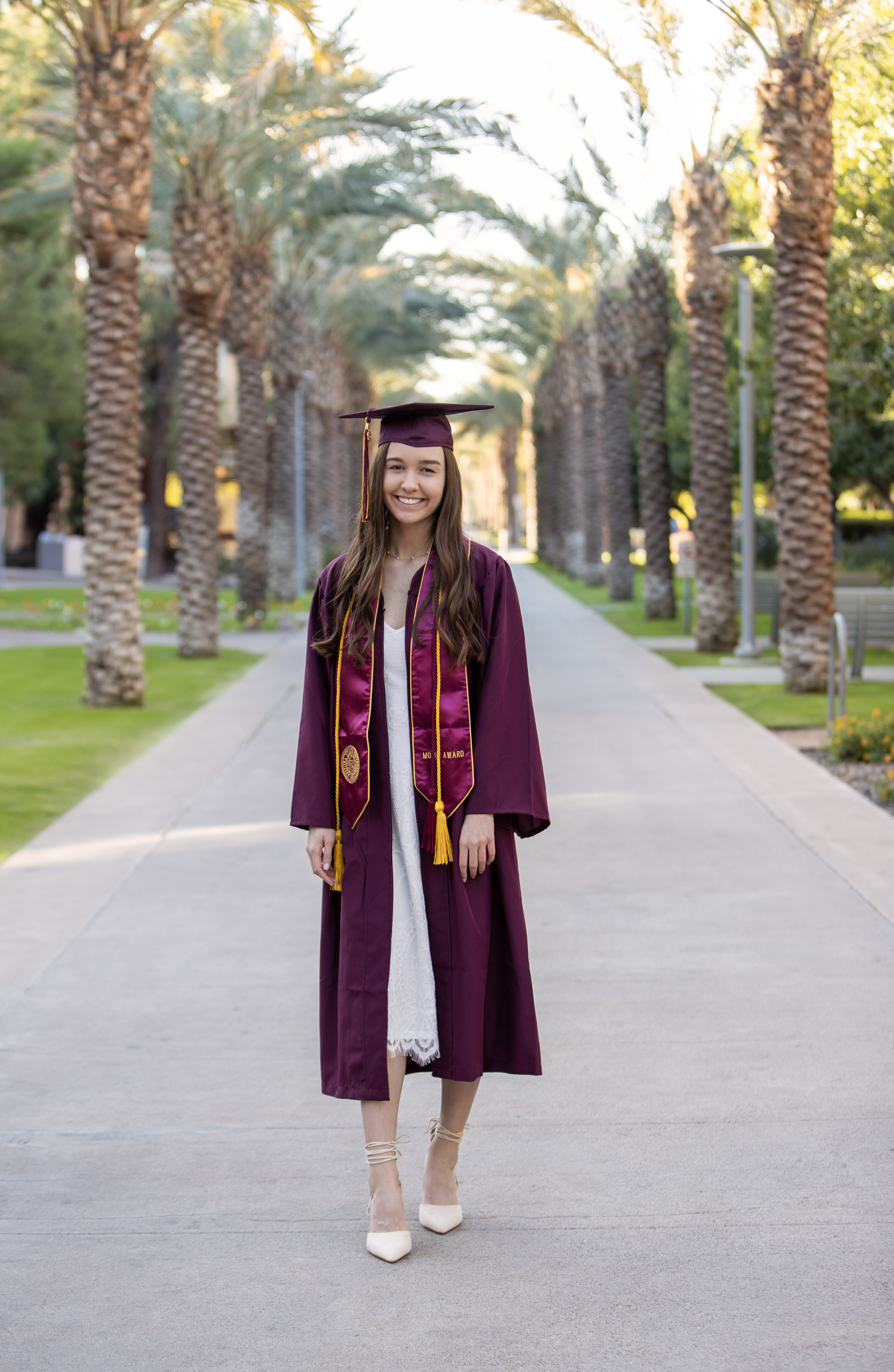 Graduate Claire Muranaka poses in her cap and gown on the palm walk at ASU.