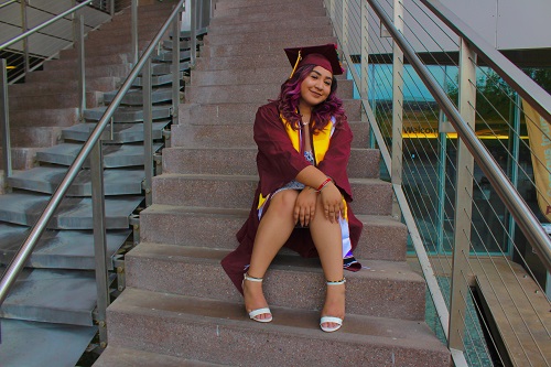 Gabriella Acosta in her ASU cap and gown sitting on steps