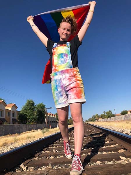 ASU student holds up a pride flag walking on train tracks