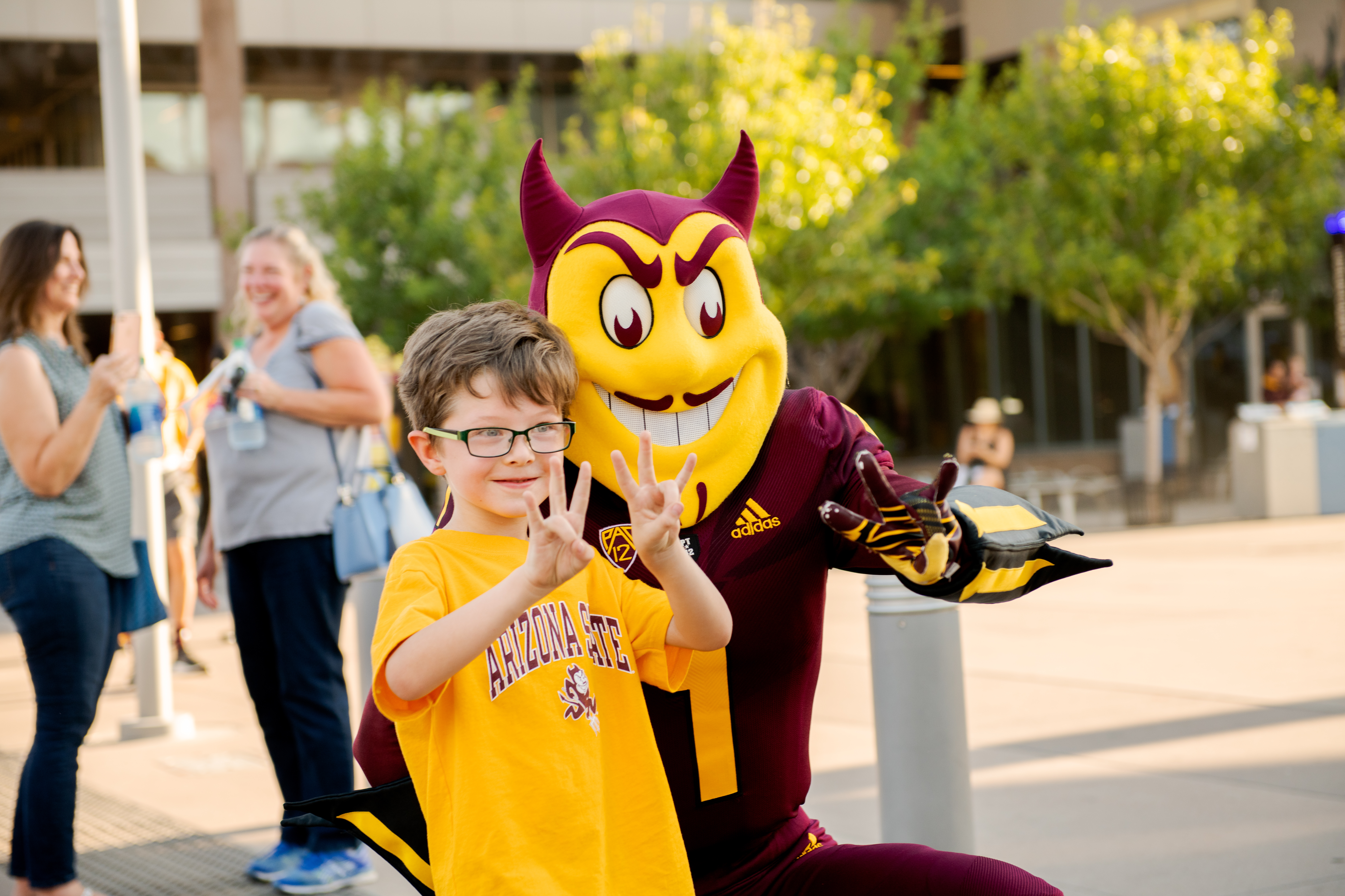 Young child in ASU gear and sparky put their "forks up." 