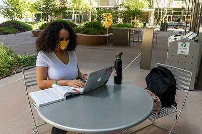 Student in a mask sitting in front of a laptop outside on ASU's Tempe campus