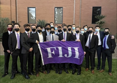 About 30 young men in suits and masks with a purple flag that says FIJI