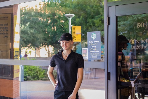 Kylie Flynn in her Starbucks uniform standing in front of the W. P. Carey Starbucks at ASU's Tempe campus
