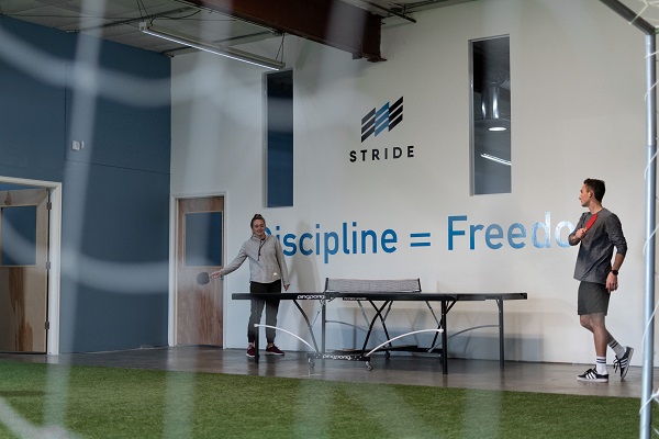 Two people playing ping pong at the Stride Learning center in front of a wall that says discipline = freedom